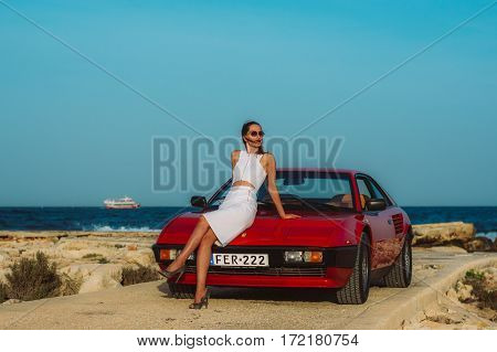 Young Beautiful Girl In Sunglasses Sitting On The Hood Of The Red Ferrari