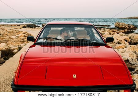 Young Girl In White Dress And Man Kissing On The Front Seats Of The Red Ferrari