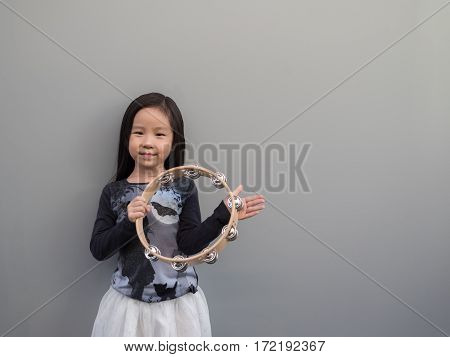 Little Asian Child Play The Tambourine, Gray Background