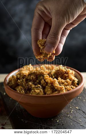 closeup of a young man eating couscous with his fingers from an earthenware casserole placed on a rustic wooden table