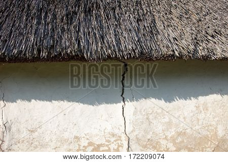 Old cracked wall of the wattle and daub house under the thatched roof. Old Ukrainian architecture.