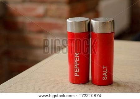 Red plastic salt cellar and pepperbox on a wooden table on loft brickwall background faded colors