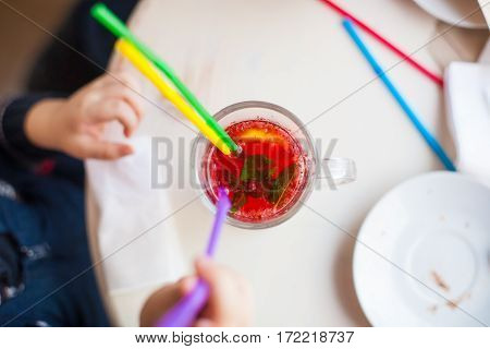 Tea from cowberry and cranberry with mint and lemon in the transparent mug stands on a white wooden table in glass with colored straws.
