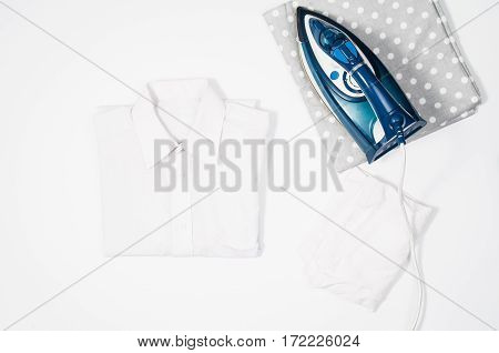 Female hand ironing clothes top view isolated on white background. Young woman with iron ironing man's shirt seen from above during housework. Blue iron on white table.