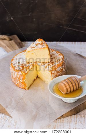 Soft cheese with cut off slice creamy texture orange rind with mold French German Alps honey dipper top view rustic kitchen interior