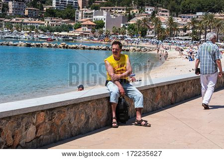 PORT DE SOLLER SPAIN - JUNE 02 2016: Tourist on the wall of the beach promenade of Port de Soller in Mallorca Spain.