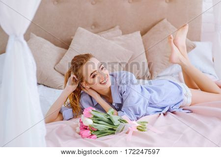beautiful young girl with bouquet of pink and white tulips lying on the bed