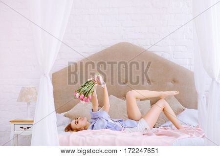 beautiful woman with white and pink tulips smiling on the bed