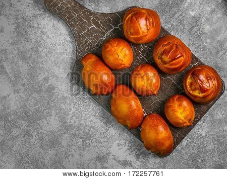 Assortment fresh patties bread buns in wooden board on gray concrete background. Fresh patties bread bun round and oval-shaped with stuffing. Top view from above and copy space.