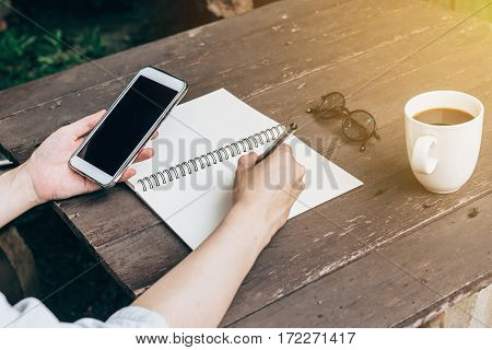Hand Woman Writing Notebook And Holding Phone On Wood Table Backhround With Vintage Toned.