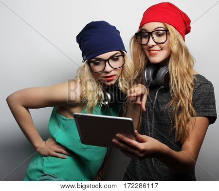 two hipster girls friends use digital tablet, studio shot over gray vackground