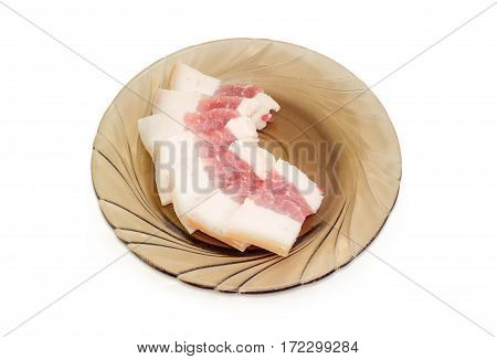 Uncooked sliced pork fatback with a skin and layer of meat on the glass saucer on a light background