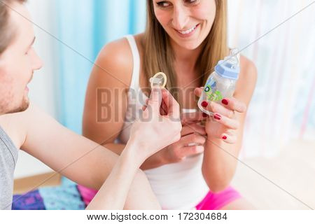 Young woman objectifies family planning for her boyfriend by contrasting condom and baby bottle