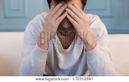 Being desperate. Sad cheerless young man sitting and covering his face while thinking about his problems