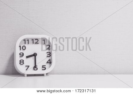 Closeup white clock for decorate show half past eight or 8:30 a.m. on white wood desk and cream wallpaper textured background in black and white tone with copy space