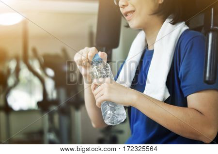 Asian woman holding bottle of water for drink after workout in the gym.