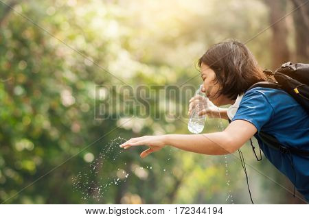 Close up Asian woman hiker pouring water from bottle on her face with nature background. copy space. Traveler.
