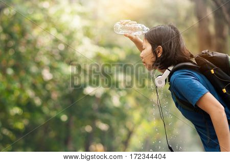 Close up Asian woman hiker pouring water from bottle on her face with nature background. copy space. Traveler.