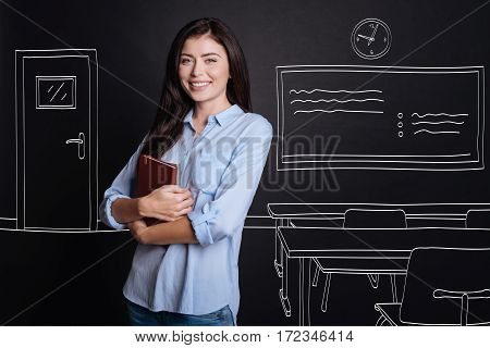My workign space. heerful diligent professional woman holding notebook and expressing gladness while standing in the classroom
