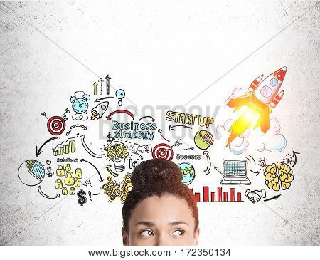 Close up of a head of an African American girl standing near a concrete wall with a colorful start up sketch.