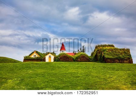 The village of houses covered with turf and grass. Church bell tower with red gabled roof. Ethnographic Museum-estate Glaumbaer, Iceland. The concept of the historical and cultural tourism