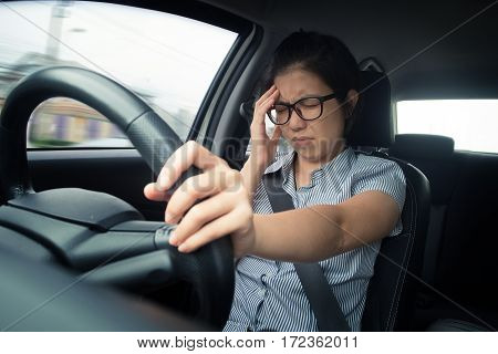 Asian glasses business woman having headache from migraine while she driving a car with bad traffic jam on rush hours. Illness exhausted disease tired for overworked concept.