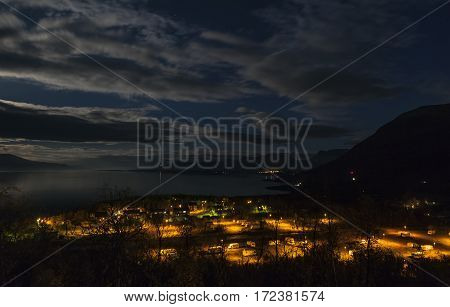 View, outlook from a hill above Bjorkliden, Lapland. Lapporten in the background. Nightfall and moonshine. Village in light, lake behind.