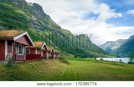Red wooden houses with grass on it's roofs. Norwegian camping near the popular touristic attraction - Briksdalsbreen glacier, Norway.