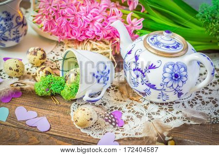 Spring floral still life with hyacinth. Blue teapot, cup, moss, feathers and quail eggs on wooden background