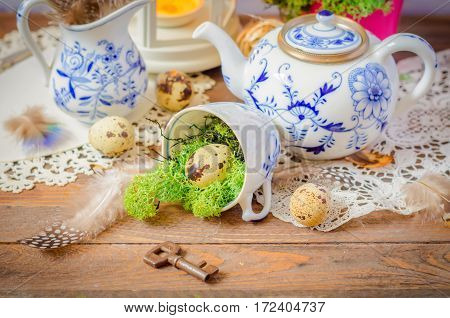 Spring floral still life with hyacinth. Blue teapot, cup, moss. Lantern, feathers and quail eggs on wooden background