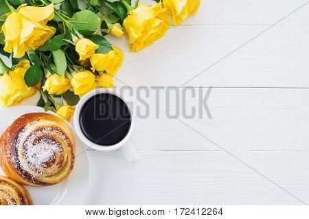 Cup of coffee with bouquet of yellow roses flat lay top view. Two spiral tasty buns with coconut chips cup of black coffee and bouquet of yellow roses. Delicious breakfast sweet rolls and coffee.