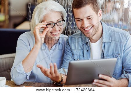 Full of joy. Cheerful content smiling woman aged woman and her grandson using tablet