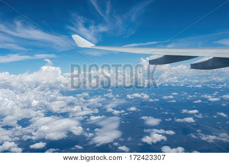 Plane flying high above the clouds. Some hills and vegetation can be seen below.