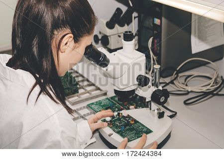 Beautiful female computer expert professional technician examining board computer in a laboratory in a factory. Troubleshooting. Technical support. Engineering. Manufacturing.