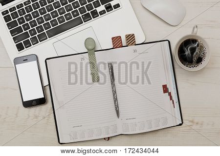 Some business accessories - diary with funny bookmarks laptop with a mouse cell phone and a cup of coffee on wooden table