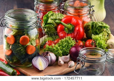 Jars With Marinated Food And Raw Vegetables On Cutting Board