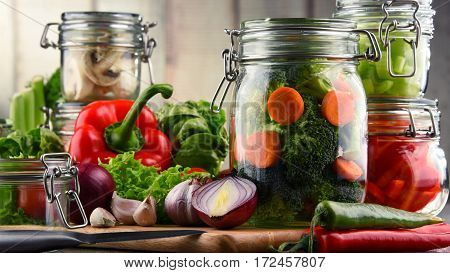 Jars With Marinated Food And Raw Vegetables On Cutting Board
