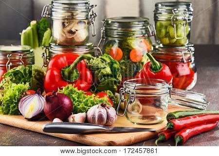Jars With Marinated Food And Raw Vegetables On Cutting Board