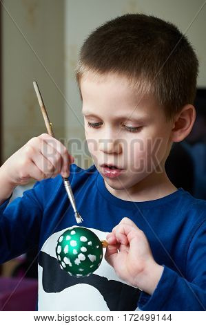 The boy paints on Christmas ball toy