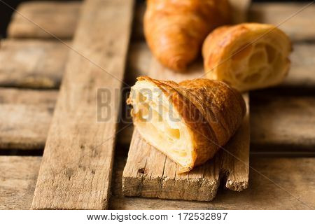 Fresh croissant cut in half with flaky pastry inside visible on aged wood backgroundclose upkinfolk minimalistic