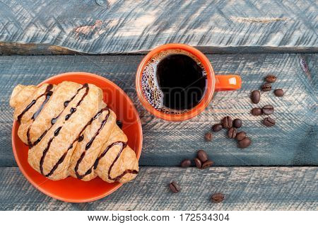 Fresh french croissant and coffee cup on old wooden table. Espresso and coffee beans on table. Top view