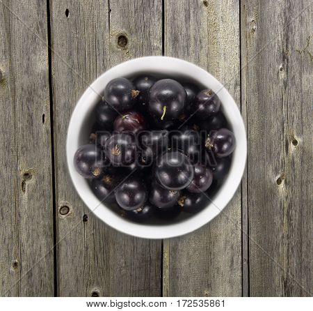 Black currants in a white ceramic bowl. Top view. Ripe and tasty currants on a wooden background. Black currants on wooden table with copy space
