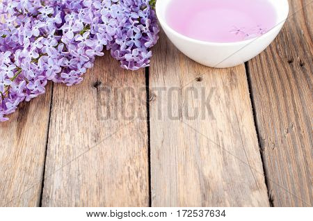 Spa background. Blossoming lilac and bowl with essential oil or flower hydrolat.