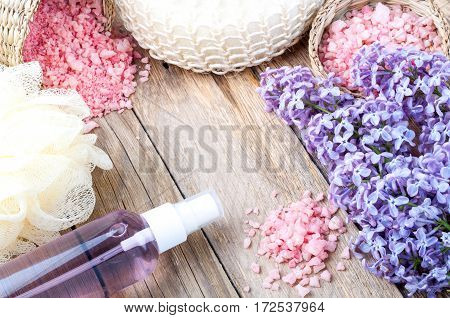 Spa background with blossoming lilac flowers and bottle of aroma oil or flower hydrolat cosmetic soap sea salt and accessories. Copy space