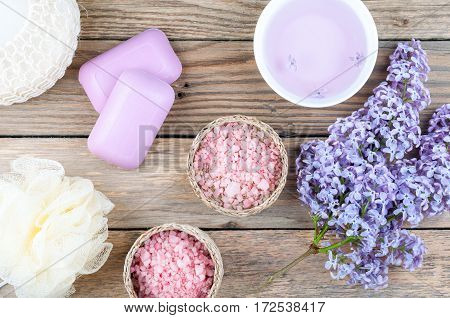 Spa background with blossoming lilac flowers and bowl with essential oil or flower hydrolat aroma cosmetic soap sea salt and accessories on rustic wooden background