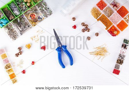 Process of making handmade jewelry. Boxes with beads pliers threads equipment and accessories for needlework on wooden table. Top view