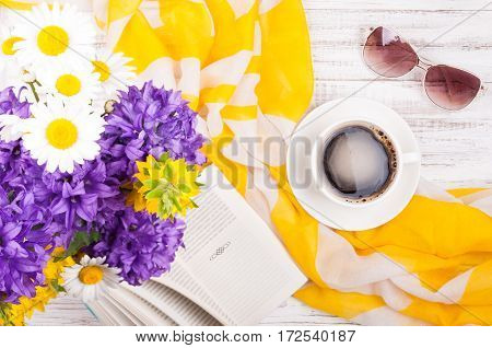 Cup of coffee book bouquet of flowers womans accessories sunglasses and neckerchief on wooden background. Summer rest concept background. Top view