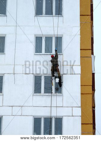 Industrial climber in helmet and uniform puttying wall on height. Risky job. Extreme work. Worker alpinist.