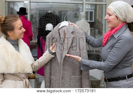 Customer selecting Jacket at Clothing Department Store talking with Saleslady who explains features and trying to convince to make Purchase Shop Interior with many Items and Windows on Background.