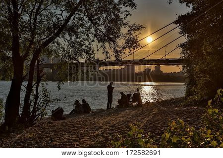 People relax on the river bank on zakate.Vdaleke sun sets over the horizon